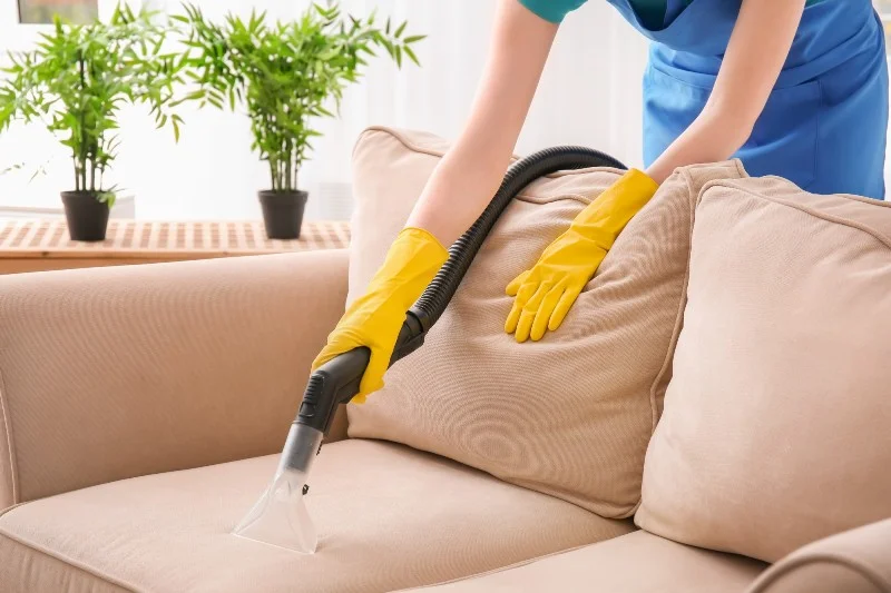 Woman cleaning couch with vacuum cleaner at home